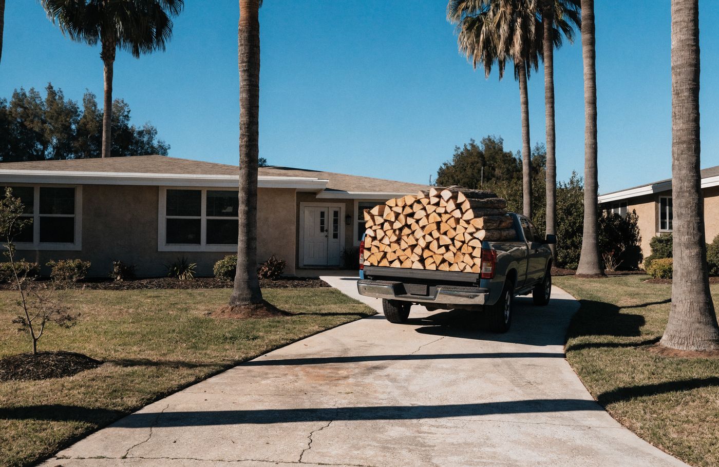 A pickup loaded with neatly stacked split firewood on a Southern California driveway
